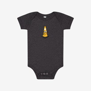 May include: A charcoal grey short-sleeve bodysuit featuring a centered graphic of a yellow traffic cone with a white reflective stripe and a small sign that reads HOIST THE CONE in black text, set on a black square base.