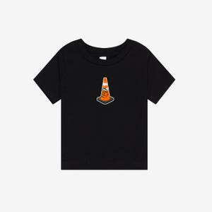 K&ouml;nnte beinhalten: Ein schwarzes T-Shirt mit kurzen &Auml;rmeln und einer mittigen Grafik eines orange-wei&szlig;en Verkehrskegels. Der Kegel hat ein kleines rechteckiges Etikett auf der Vorderseite mit dem Text "HOIST THE CONE" in schwarzen Buchstaben auf orangefarbenem Grund.