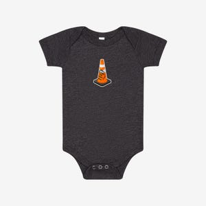 May include: A dark charcoal grey short-sleeve baby bodysuit featuring a centered graphic of an orange traffic cone with a white stripe. The cone includes a small rectangular sign with the black text HOIST THE CONE printed on its front surface.