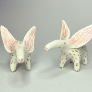 May include: Two ceramic animal figurines. The figurines are white with brown spots and large, pink-lined ears. They have long snouts and small, black eyes. The figurines are standing on four legs.