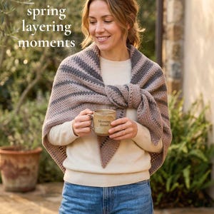 May include: A woman wearing a beige sweater and blue jeans, with a striped shawl in shades of gray and beige. She holds a ceramic mug with the words "Morning Ritual" printed on it. The text "excited for spring layering moments" is in the upper left corner.