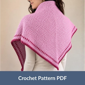 Puede incluir: Un chal triangular de ganchillo que presenta un cuerpo principal de color rosa claro texturizado con un borde de color magenta oscuro. El chal está drapeado sobre los hombros e incluye un patrón de puntos repetitivo con un detalle de borde.
