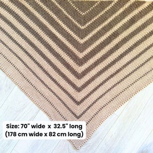 May include: A handmade crochet shawl in a chevron pattern. The shawl features alternating stripes of beige and brown. The dimensions are 70 inches wide and 32.5 inches long.