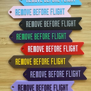 May include: A collection of colorful, arrow-shaped tags with the text "REMOVE BEFORE FLIGHT" in white. The tags are in various colors, including blue, pink, black, purple, red, brown, and lavender.