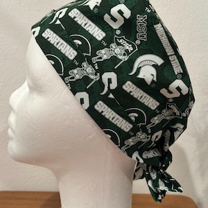 Peut inclure: Un bonnet de chirurgien vert et blanc à motifs avec les inscriptions "SPARTANS", "MSU" et "MICHIGAN STATE". Le bonnet présente un motif répété de la lettre "S", de casques spartiate et de figurines spartiate. Le bonnet est noué à l'arrière.