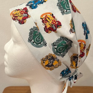 May include: White fabric head covering featuring repeating crests of Hogwarts houses: Gryffindor, Slytherin, Hufflepuff, and Ravenclaw. The head covering is tied at the back. The crests are in red, gold, green, and blue.