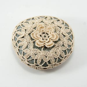 May include: A round stone covered in a crocheted lace doily with a delicate white flower in the center.
