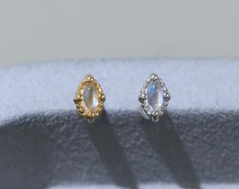 May include: Two small stud earrings, one in gold and one in silver, each featuring a marquise-shaped moonstone set within a beaded metal frame. The earrings are positioned side-by-side, displaying a delicate design with a central iridescent stone.