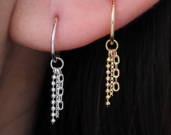 May include: Close-up of two dangling earrings. One is silver with a chain of small beads, and the other is gold with a chain of small oval links. A gold hoop earring is also visible.