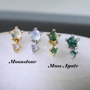 Può includere: Quattro orecchini a bottone con pietre preziose su una pietra bianca. Due paia sono etichettati "Moonstone" e due "Moss Agate". Gli orecchini hanno una parte superiore a forma di stella con una gemma pendente. Gli orecchini sono di colore oro e argento.