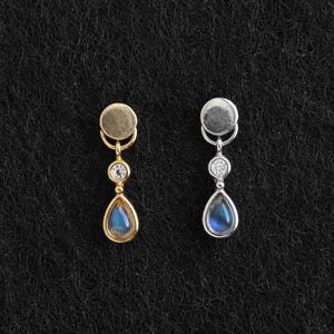May include: Two drop earrings, one in gold tone and one in silver tone. Each earring features a circular stud top, a small clear round stone in the center, and a dangling teardrop-shaped blue stone at the bottom, creating a delicate vertical design.