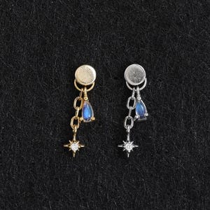 Peut inclure: Deux boucles d'oreilles à tige, une dorée et une argentée, composées d'un sommet circulaire, d'une courte chaîne, d'une petite pierre bleue en forme de goutte et d'une breloque en forme d'étoile avec une minuscule pierre claire au centre.