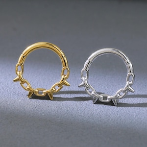 May include: Two hoop earrings, one gold-toned and one silver-toned, each featuring a chain-like design with small, pointed spikes. The earrings are displayed on a gray surface, showcasing their contrasting colors and textures.