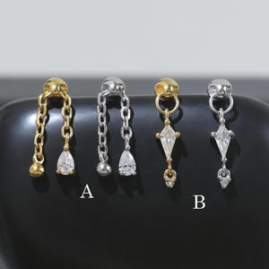 May include: Four earrings displayed on a black surface. Two pairs are gold-toned, one with a chain and teardrop gem, the other with a diamond-shaped gem. The other two pairs are silver-toned, with similar designs. The earrings are labeled A and B.