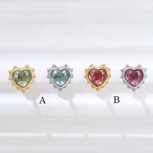 May include: Four heart-shaped stud earrings arranged in a row. The first is gold with a green stone, the second is silver with a blue stone, the third is gold with a pink stone, and the fourth is silver with a dark pink stone. Labels A and B appear.