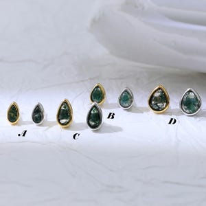 May include: A collection of teardrop-shaped stud earrings. The earrings feature a green stone with varying shades and patterns, set in gold or silver-toned metal. The earrings are displayed on a white surface.