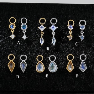 May include: A collection of delicate earrings displayed on a black surface. The earrings feature various designs, including teardrop, diamond, and circular shapes, with gold and silver metal finishes. Some earrings have blue and clear gemstones.