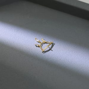 May include: A gold-colored earring with a delicate design. The earring features a series of small, clear, teardrop-shaped stones connected by fine chains. The earring post is visible, and the overall design is elegant and minimalist.