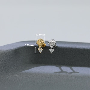Puede incluir: Dos pendientes de bot&oacute;n, uno dorado y otro plateado, cada uno con una parte superior en forma de concha y una gema transparente colgante. El pendiente dorado mide 7,0 mm de largo y 3,4 mm de ancho.