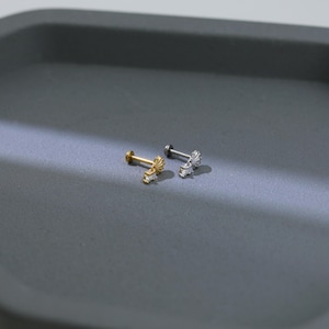 Puede incluir: Dos pendientes peque&ntilde;os y decorativos. Uno es dorado con un dise&ntilde;o de sol y peque&ntilde;as piedras transparentes. El otro es plateado con un dise&ntilde;o similar. Ambos pendientes tienen un poste y una parte trasera plana.
