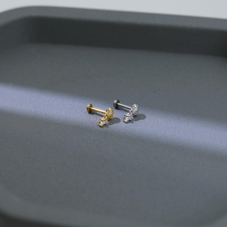 Puede incluir: Dos pendientes peque&ntilde;os y decorativos. Uno es dorado con un dise&ntilde;o de sol y peque&ntilde;as piedras transparentes. El otro es plateado con un dise&ntilde;o similar. Ambos pendientes tienen un poste y una parte trasera plana.