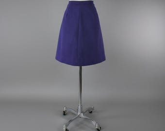 May include: A-line skirt in a deep purple hue, displayed on a mannequin. The skirt has a classic design with a fitted waist and a flared silhouette. The fabric appears to be a smooth, solid material. The skirt is mounted on a chrome stand with wheels.
