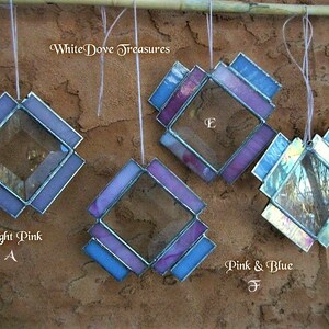 May include: Four stained glass diamond-shaped ornaments with different color combinations. The ornaments are hanging from a wooden dowel. The colors are light pink, purple, blue, and pink and blue. The text "White Dove Treasures" is visible at the top of the image.