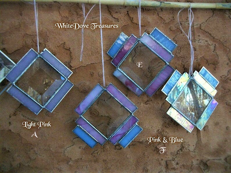 May include: Four stained glass diamond-shaped ornaments with different color combinations. The ornaments are hanging from a wooden dowel. The colors are light pink, purple, blue, and pink and blue. The text "White Dove Treasures" is visible at the top of the image.
