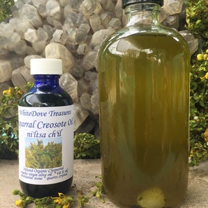 May include: Two glass bottles of oil, one clear and one dark green, with labels that read "White Dove Treasures parral Creosote Oil ni'ltsa ch'il" and "Infused Organic Chaparral virgin olive oil vit E oil *quartz crystal enturine stone".
