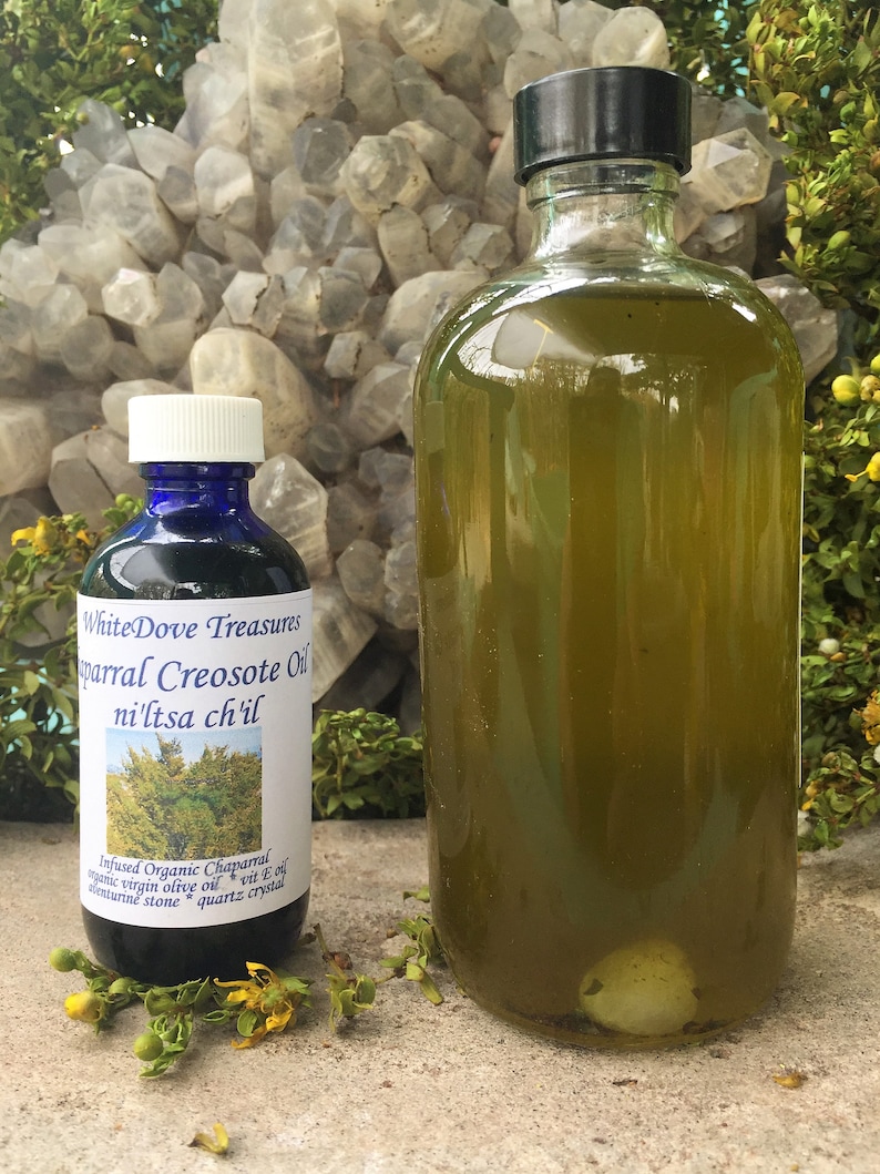 May include: Two glass bottles of oil, one clear and one dark green, with labels that read "White Dove Treasures parral Creosote Oil ni'ltsa ch'il" and "Infused Organic Chaparral virgin olive oil vit E oil *quartz crystal enturine stone".