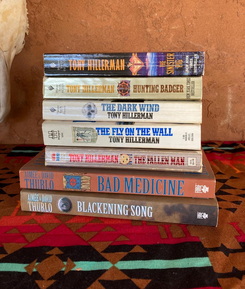 Pode incluir: Uma pilha de sete livros com t&iacute;tulos como "The Sinister Rig" e "Bad Medicine". Os livros est&atilde;o empilhados sobre um tecido estampado com desenhos geom&eacute;tricos vermelhos, castanhos e pretos. As lombadas mostram os nomes dos autores e os t&iacute;tulos.
