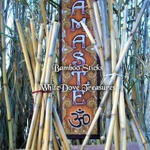 May include: A bundle of natural bamboo sticks tied together with red string, resting on a brown surface. A sign with the word "Namaste" and the symbol "Om" is visible in the background. Bamboo sticks for crafts, meditation, or home decor.