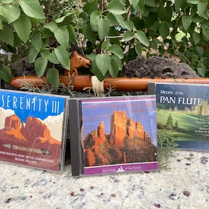 May include: Three CD cases with nature-themed artwork. The CDs are titled "Serenity III", "Sedona Sounds", and "Moods of the Pan Flute". A wooden flute and a carved wooden horse are in the background.