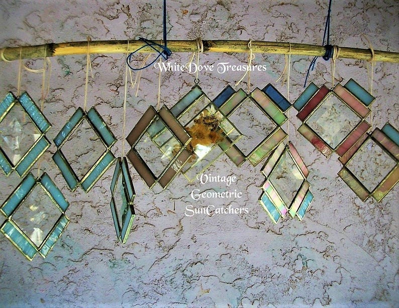 May include: A collection of vintage geometric stained glass suncatchers hanging from a bamboo rod. The suncatchers are made of various colors of glass, including blue, green, pink, and brown. The text "White Dove Treasures" and "Vintage Geometric Suncatchers" is visible in the image.