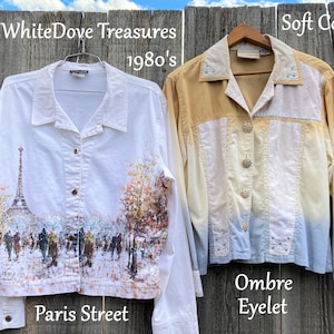 May include: Two long-sleeved button-up shirts. The white shirt has a print of the Eiffel Tower and a Parisian street scene. The text "Paris Street" is below the image. The text "WhiteDove Treasures 1980's" is above the image. The second shirt is a soft yellow, white, and blue ombre with eyelet detailing. The text "Soft Cotton XL" is above the image. The text "Ombre Eyelet" is below the image.