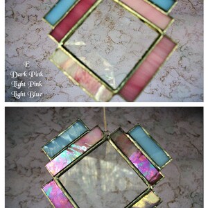 May include: A stained glass window hanging with a diamond shape. The window is made of clear glass with a border of pink and light blue glass.