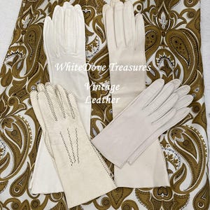 May include: Four pairs of vintage cream-colored leather gloves are displayed against a paisley patterned background. The gloves vary in length and style, with some featuring decorative stitching. The text "White Dove Treasures Vintage Leather" is visible.