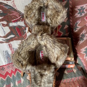 Pode incluir: Chinelos estilo mocassim castanhos com acabamento em pele sint&eacute;tica. Os chinelos t&ecirc;m um aspeto semelhante a camur&ccedil;a e apresentam o nome da marca "BONGO" numa etiqueta. O acabamento em pele &eacute; uma mistura de cores castanhas e bege. Os chinelos s&atilde;o projetados para uso em ambientes internos.