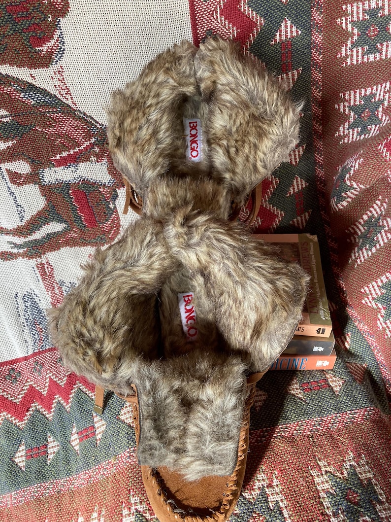 Pode incluir: Chinelos estilo mocassim castanhos com acabamento em pele sint&eacute;tica. Os chinelos t&ecirc;m um aspeto semelhante a camur&ccedil;a e apresentam o nome da marca "BONGO" numa etiqueta. O acabamento em pele &eacute; uma mistura de cores castanhas e bege. Os chinelos s&atilde;o projetados para uso em ambientes internos.