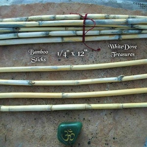 Op de afbeelding: Een bundel natuurlijke bamboestokken van 6,35 mm dik en 30,48 cm lang. De stokken zijn lichtbruin met een witte coating. De tekst "Bamboo Sticks" en "White Dove Treasures" is zichtbaar in de afbeelding.