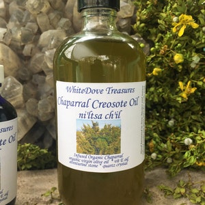 May include: A glass bottle of Chaparral Creosote Oil infused with organic virgin olive oil, aventurine stone, and quartz crystal. The label reads "WhiteDove Treasures Chaparral Creosote Oil ni'ltsa ch'il".