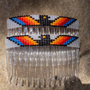 May include: A white plastic hair comb with two beaded designs. The designs are of an eagle with black, orange, red, and blue beads.