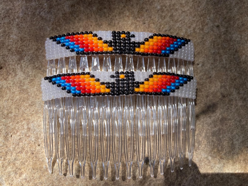 May include: A white plastic hair comb with two beaded designs. The designs are of an eagle with black, orange, red, and blue beads.