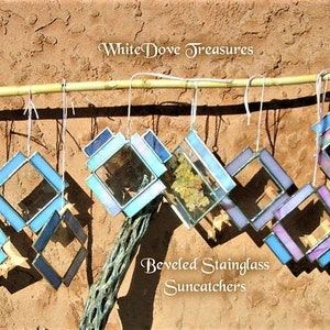 May include: A collection of eight beveled stained glass suncatchers hanging from a bamboo rod. The suncatchers are in shades of blue, purple, and white. The text "WhiteDove Treasures" and "Beveled Stainedglass Suncatchers" is visible in the image.