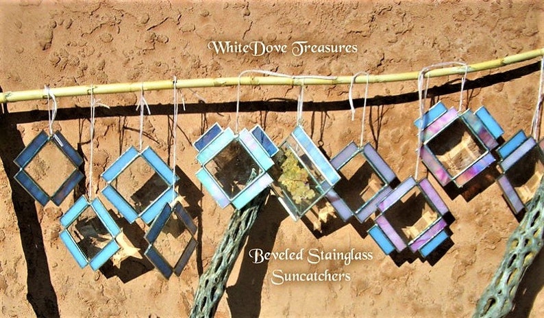 May include: A collection of eight beveled stained glass suncatchers hanging from a bamboo rod. The suncatchers are in shades of blue, purple, and white. The text "WhiteDove Treasures" and "Beveled Stainedglass Suncatchers" is visible in the image.