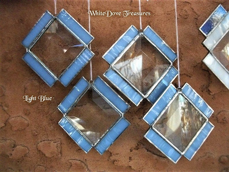 May include: Five light blue diamond-shaped stained glass ornaments with clear glass centers. The ornaments are hanging from white strings. The text "White Dove Treasures" is visible in the top right corner of the image. The text "Light Blue" is visible in the bottom left corner of the image.