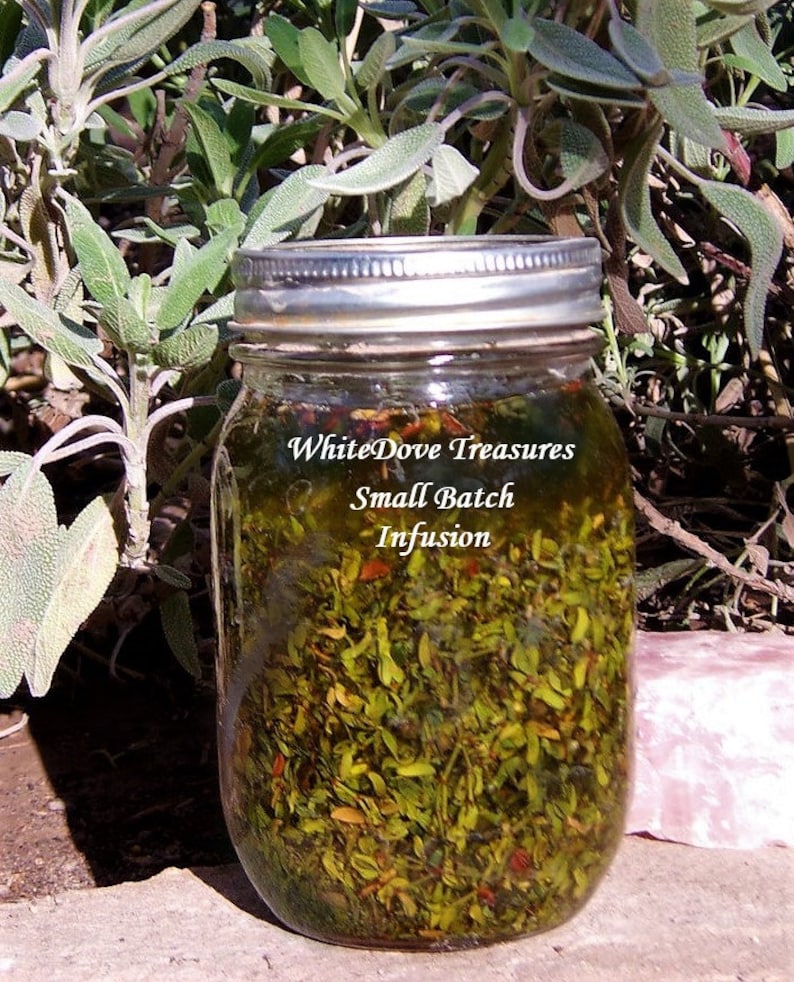 May include: A glass jar filled with green herbs and a clear liquid. The jar has a silver lid and a label that reads "WhiteDove Treasures Small Batch Infusion".