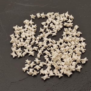 Peut inclure: Une collection de petits objets blancs cassé en forme d'os, dispersés sur une surface sombre. Les objets ressemblent à des vertèbres miniatures, potentiellement pour l'artisanat ou l'éducation. L'ensemble évoque un matériau naturel et organique.