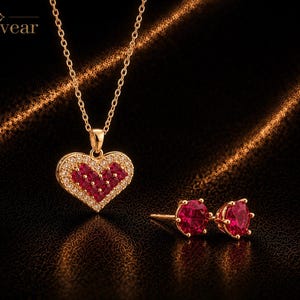 Puede incluir: Un collar de tono dorado con un colgante en forma de corazón que presenta un grupo de piedras rojas rodeadas por un halo de pequeñas piedras claras, junto con pendientes de botón redondos a juego. El texto Monvear es visible en la esquina superior.