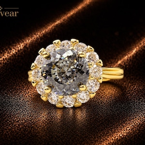 May include: A gold ring featuring a large, round, grey center stone surrounded by a halo of smaller, clear, round-cut stones. The band is made of polished gold. The text Monvear is visible in the upper left corner of the image.
